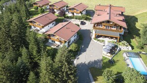 A cluster of chalet-style buildings with a central road, surrounded by dense forest and open fields. - Feriendorf-wallenburg / Enzian - Ferienwohnung für 2-4 Personen (Fieberbrunn)