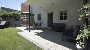A patio area with a stone wall, a table with chairs, a sofa, and a pergola. - Feriendorf-wallenburg / Enzian - Ferienwohnung für 2-4 Personen (Fieberbrunn)