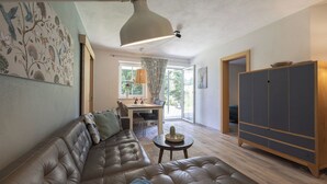 A living room with a leather sofa, a dining table, and a cabinet. - Feriendorf-wallenburg / Enzian - Ferienwohnung für 2-4 Personen (Fieberbrunn)
