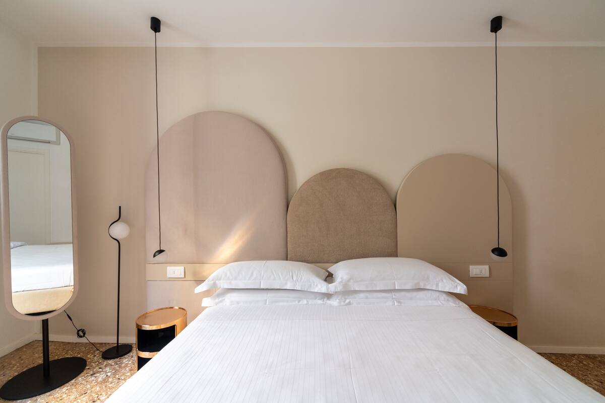 A bedroom with a large bed, a round mirror, a floor lamp, and a bedside table.