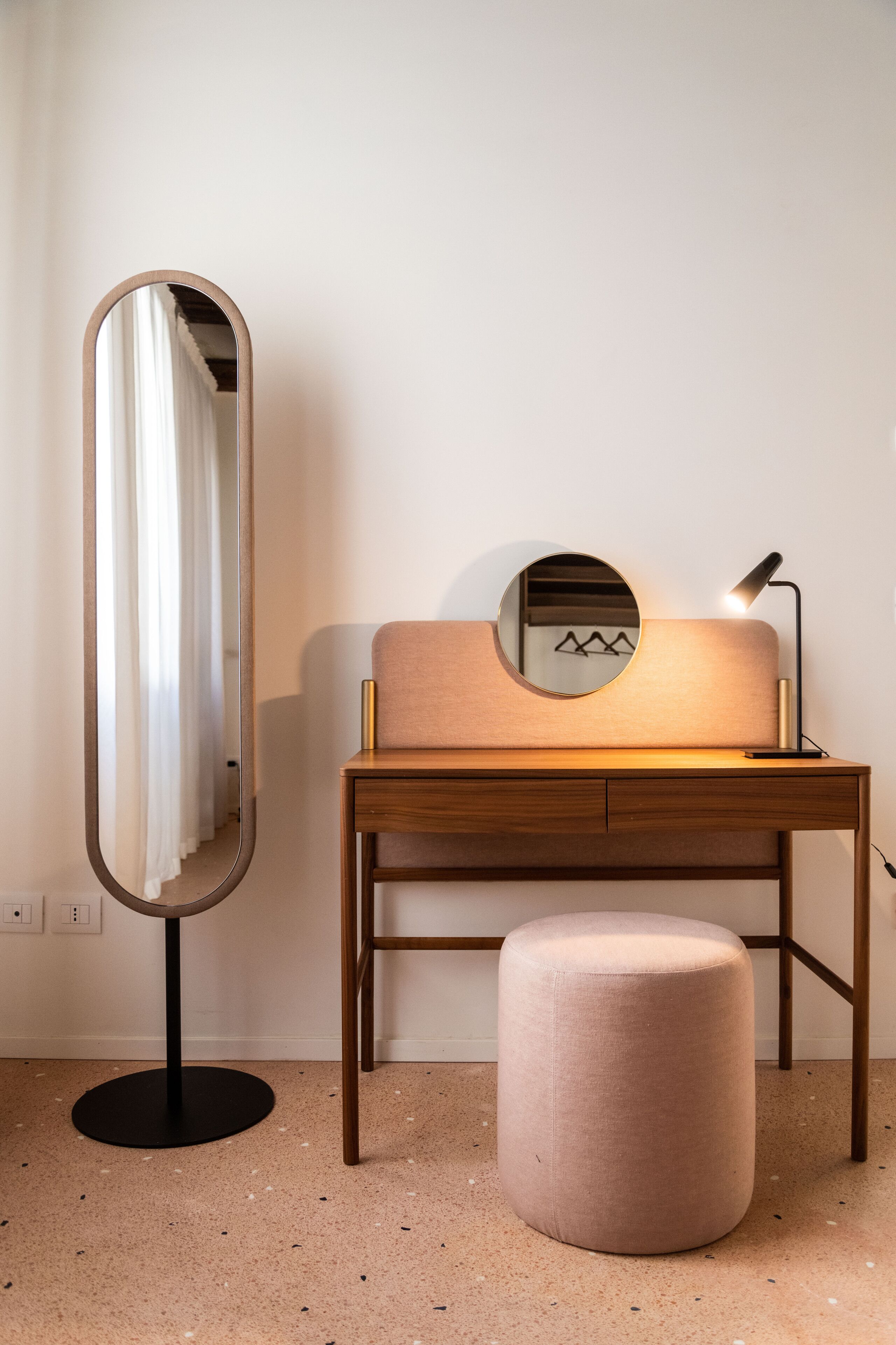 Una habitación moderna con un escritorio de madera, un espejo redondo, un taburete pequeño y una lámpara.