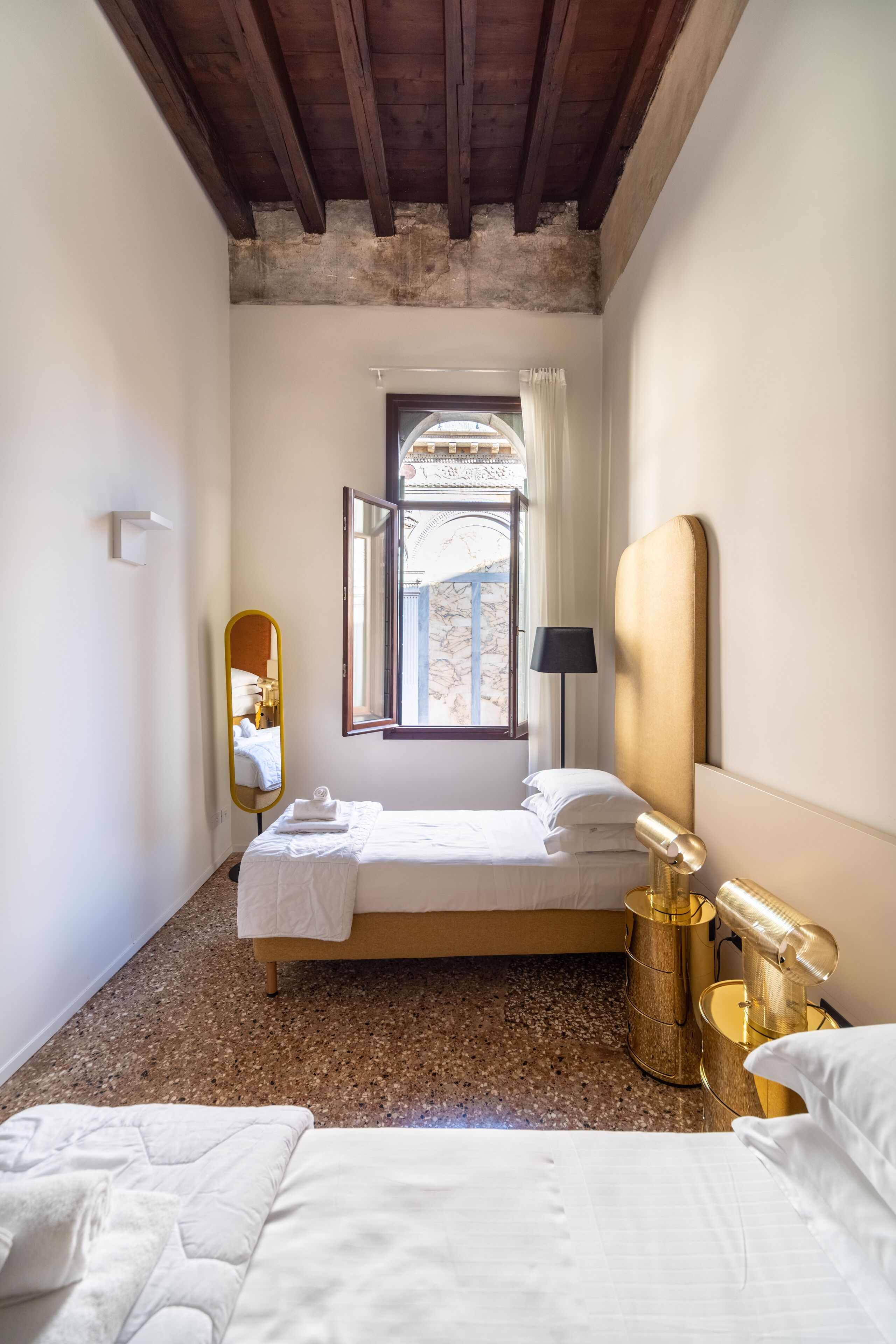 A bedroom with a bed, a bedside lamp, a mirror, and a window with curtains.