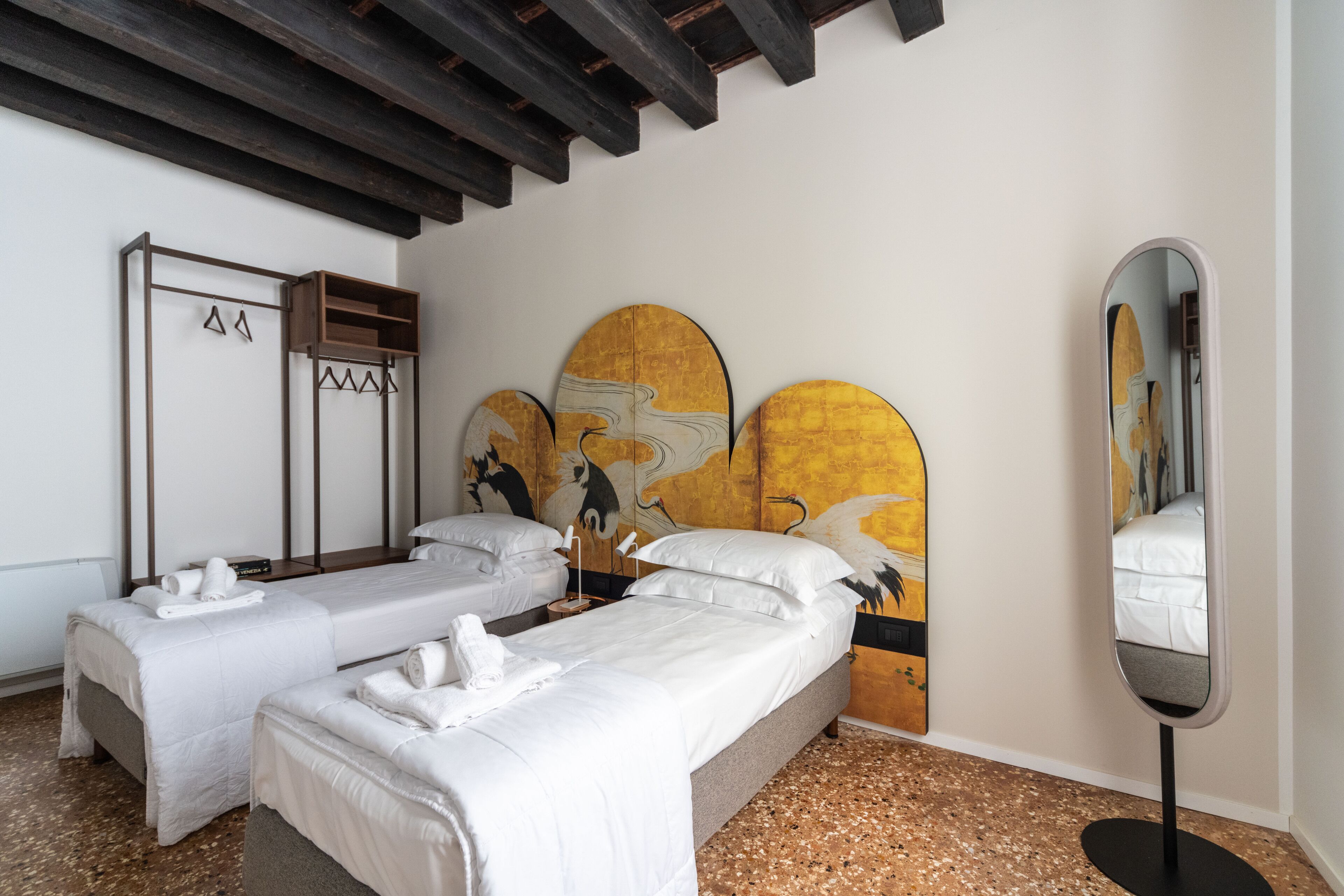 A hotel room with two beds, a wooden wardrobe, a large mirror, and a wall with a yellow and white abstract painting.