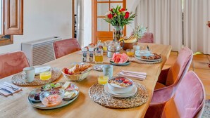 A breakfast setting with a wooden table, wicker placemats, and various breakfast items including croissants, fruit, and a vase with flowers. - Casa Llibertat (Lliber)