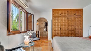 A bedroom with a bed, a chair, a table with a vase, and a wooden wardrobe. - Casa Llibertat (Lliber)