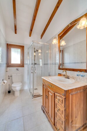 A modern bathroom with a glass shower enclosure, a wooden vanity with a large mirror, and a toilet with a bidet attachment. - Casa Llibertat (Lliber)