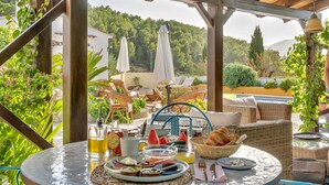 A breakfast setup with a wicker table, wicker chairs, and a view of a lush green landscape. - Casa Llibertat (Lliber)