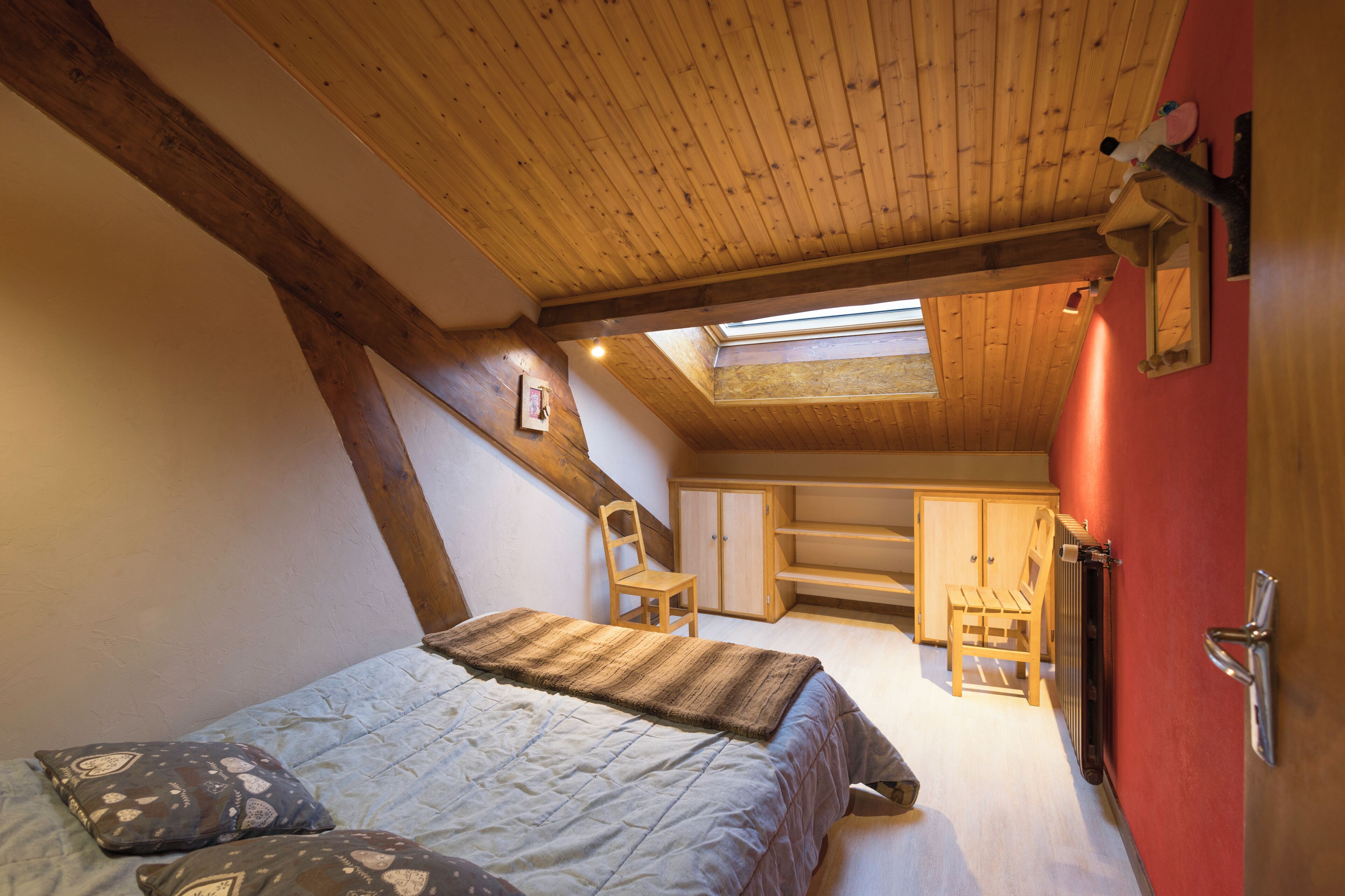 Une chambre avec un plafond en pente, un lit, une chaise, un radiateur et une armoire.
