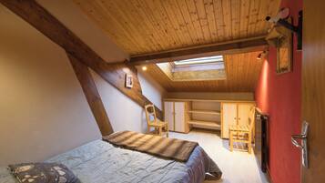Une chambre avec un plafond en pente, un lit, une chaise, un radiateur et une armoire.