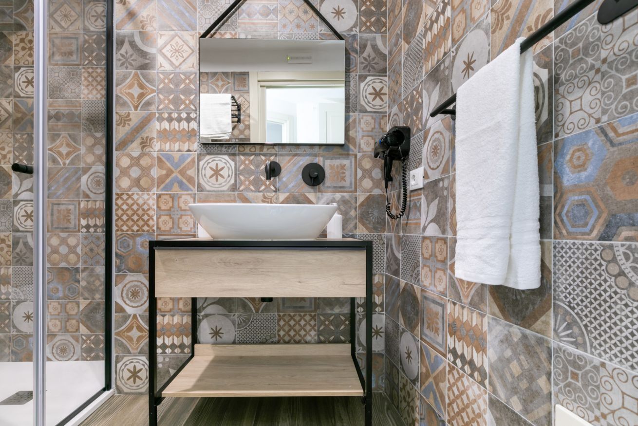 Une salle de bain avec des carreaux décorés, un lavabo blanc, un miroir, un porte-serviettes et un sèche-cheveux.