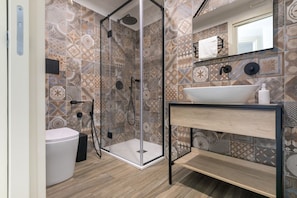 Une salle de bain avec des carreaux décorés, une douche en verre, des toilettes blanches et un lavabo avec un miroir au-dessus.