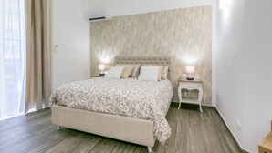 A bedroom with a large bed, two bedside tables with lamps, a window with curtains, and a textured wall. - GuestHost - Charming 60 sqm apartment, for 5 people, located on the 1st floor of a renovated period building (NO lift; 38 steps). The property is located in the center of Palermo (Restricted-Traffic Area), a few steps from the main attractions of the cit (Palermo)
