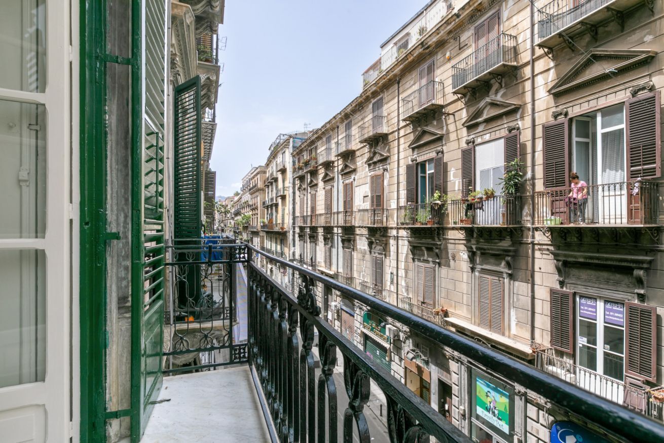 Une rue étroite bordée d’immeubles à plusieurs étages, de balcons et d’un trottoir réservé aux piétons.