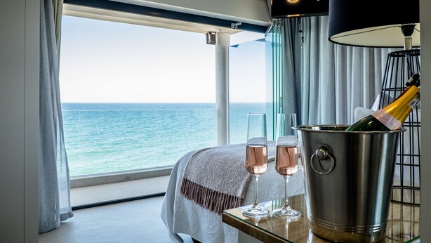 Een kamer met een groot raam met uitzicht op zee, een tafel met twee champagneglazen en een emmer met champagne.