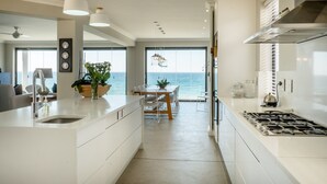 Een moderne keuken met een groot eiland, witte kastjes en uitzicht op zee.