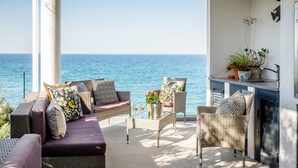 Een balkon met rieten meubilair, een plant in pot en uitzicht op zee.