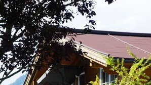 En stuga med en träbalkong, en stenmur och utsikt över grönskande kullar.