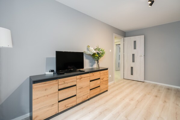 Un soggiorno moderno con una televisione a schermo piatto su un mobile in legno, un vaso con fiori e una porta sullo sfondo.