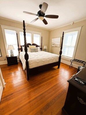 A four-poster bed with a ceiling fan, wooden flooring, and a view of the water through large windows.