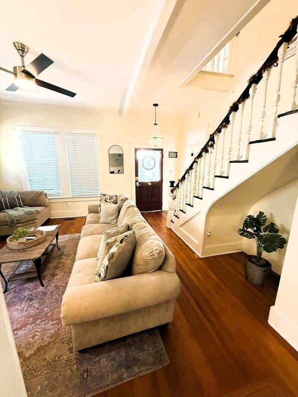 A spacious living room with a large beige sofa, a coffee table, and a staircase with a white railing.
