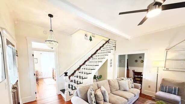 A spacious living room with a beige sofa, a coffee table, and a staircase with a railing. - The Big Sanchez - 5 BR-3BA - 1890s Charm (St. Augustine)