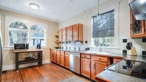 A modern kitchen with wooden cabinets, a stainless steel dishwasher, and a large window providing natural light. - The Big Sanchez - 5 BR-3BA - 1890s Charm (St. Augustine)