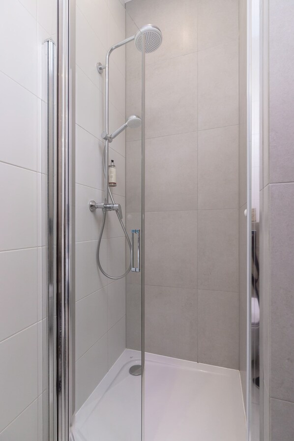 Une douche moderne dotée d’une porte en verre, d’un pommeau de douche à main et d’un robinet mural.
