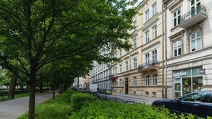 A street lined with trees and parked cars, with a building featuring a 'Zabka' store on the ground floor. - Functional Studio | Close to Market Square and Wawel Castle (Kraków)
