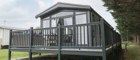 A modern mobile home with a balcony, a covered porch, and a fenced yard.