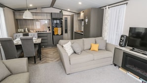 A modern living room with a sofa, TV, and fireplace. There is a dining area with a table and chairs. The kitchen is visible in the background. - 59 Finch (Scarborough)