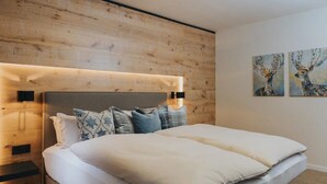A modern bedroom with a wooden headboard, a large bed with multiple pillows, and two wall-mounted paintings.