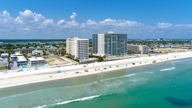 A coastal hotel with multiple buildings, a beach, and clear blue waters.