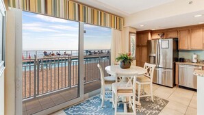 A balcony with a view of the beach, a dining area with a table and chairs, and a kitchen with wooden cabinets and modern appliances.