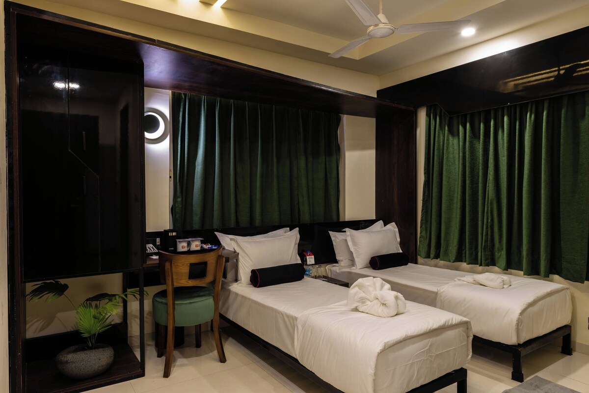 A hotel room with two single beds, a desk with a chair, a small table with a plant, and a ceiling fan.