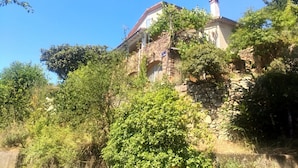 Ein Haus aus Stein mit rotem Ziegeldach, umgeben von dichtem Grün und Bäumen.