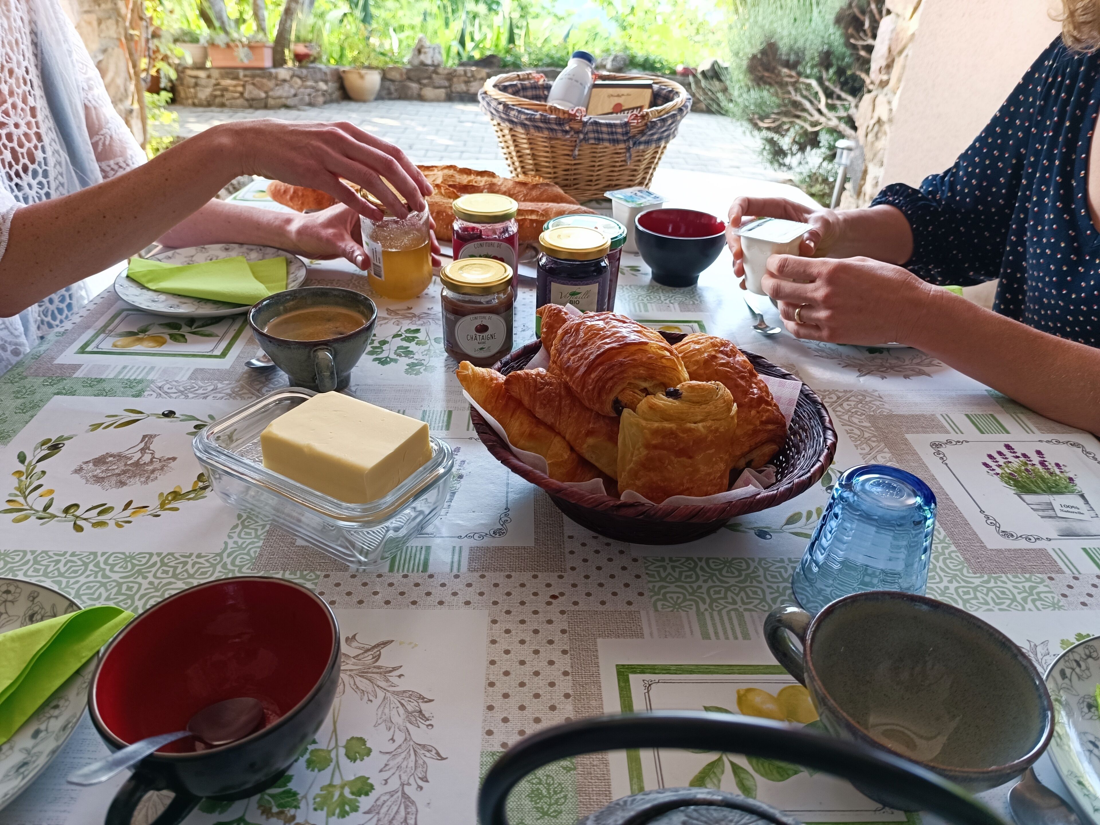 A table set with food and drinks, including croissants, butter, jam, and a basket.