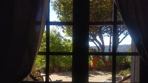 Ein Fenster mit Blick auf eine Terrasse, inklusive Tisch und Stühlen, Blumentöpfen und einer Steinmauer.