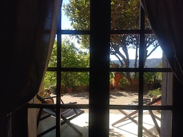 Una ventana con vistas a un patio, que incluye una mesa, sillas, plantas en macetas y un muro de piedra.
