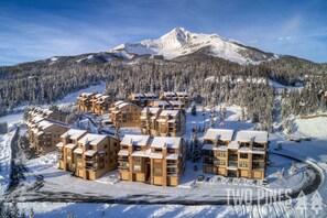 Un ensemble de bâtiments de style chalet, à plusieurs étages et dotés de balcons, entourés d’arbres couverts de neige et avec une montagne en arrière-plan.