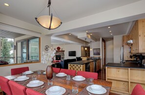 Uma sala de jantar moderna com uma mesa de madeira posta para seis pessoas, cadeiras estofadas vermelhas e um vaso com flores brancas.