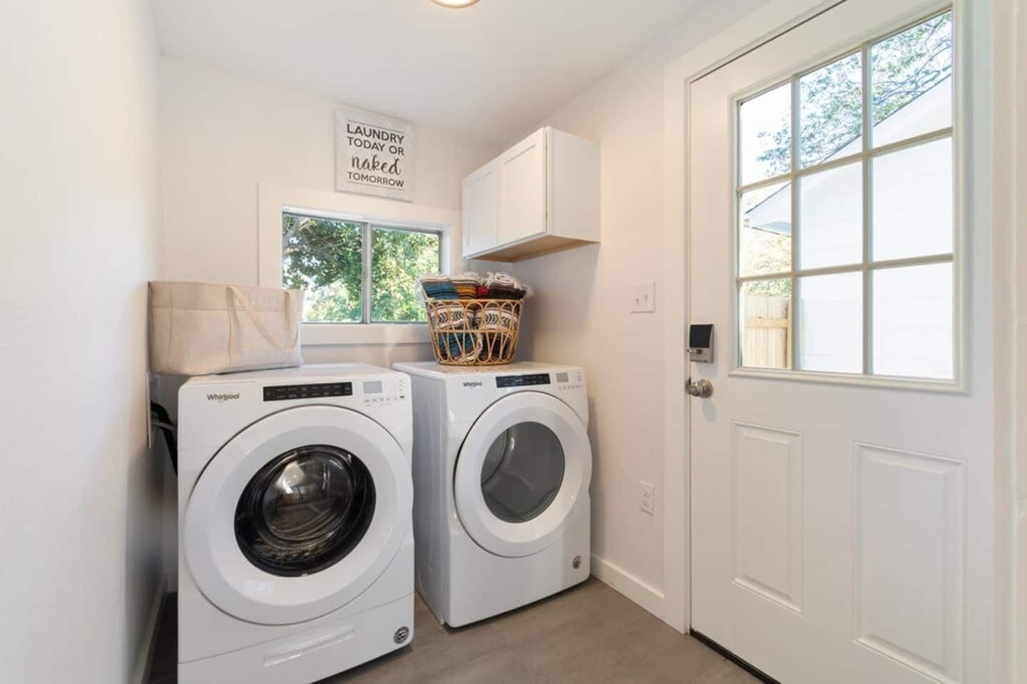 A laundry room with two front-loading washers, a basket of folded clothes, and a sign above the washers.
