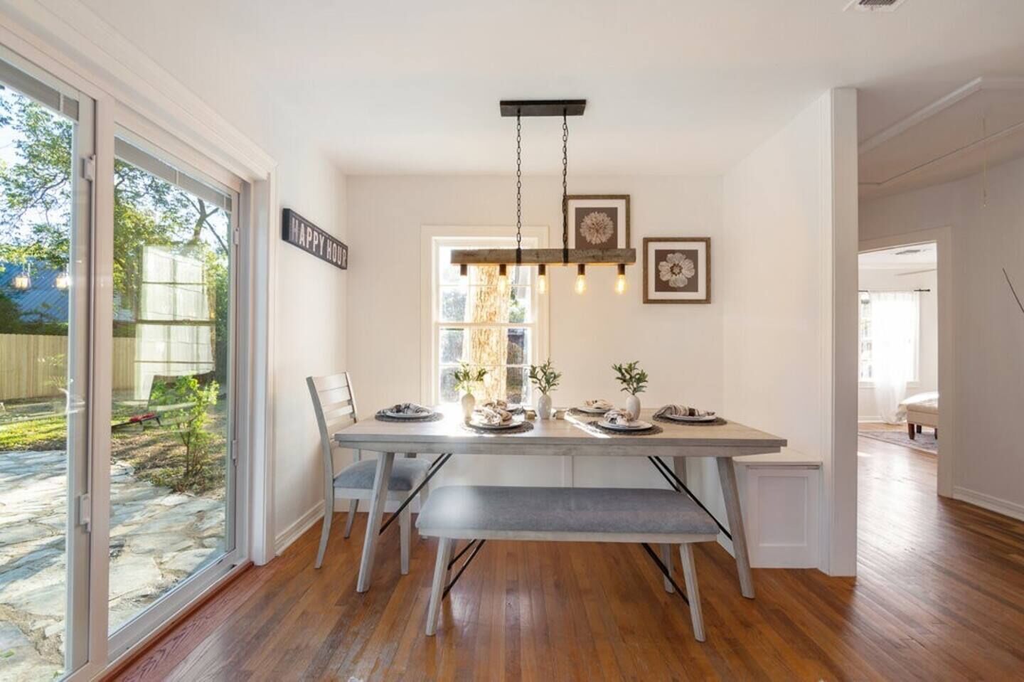 A dining area with a wooden table, benches, a hanging light fixture, and framed pictures on the wall.