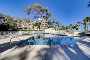 Une piscine avec des chaises longues, des palmiers et un bâtiment doté de balcons en arrière-plan.