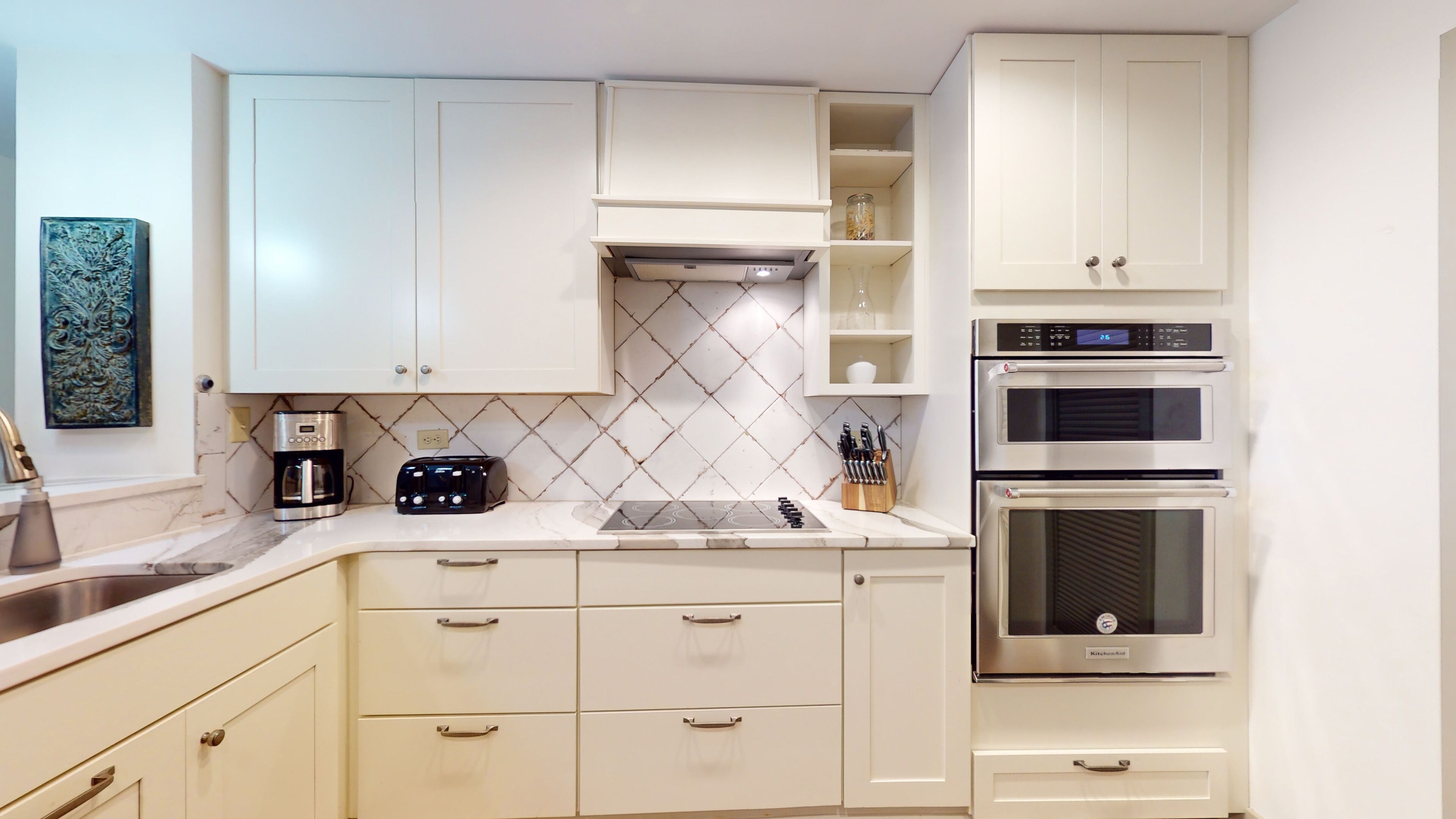 Una cocina moderna con armarios blancos, horno empotrado y cafetera.