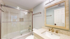 Une salle de bain moderne avec une douche à parois de verre, un lavabo blanc et un grand miroir avec un cadre doré.