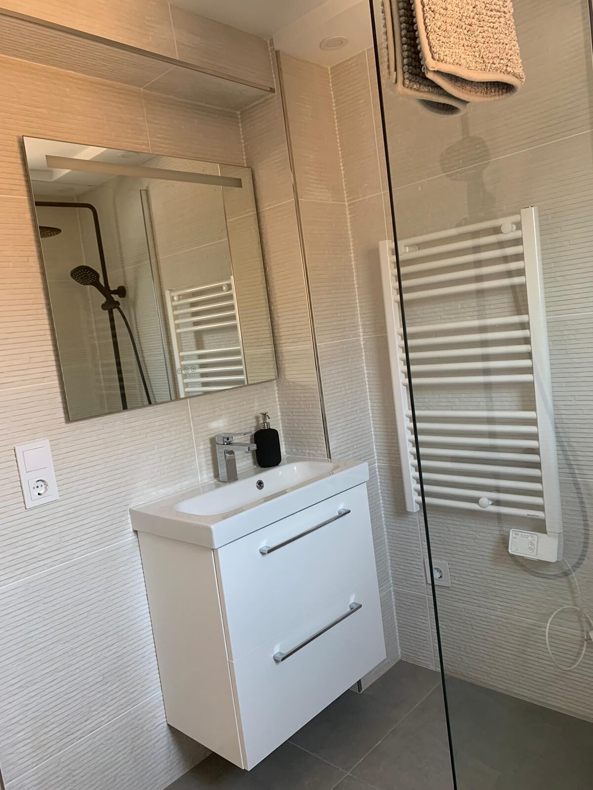 A modern bathroom with a white vanity, a large mirror, a glass shower enclosure, and a towel rack.