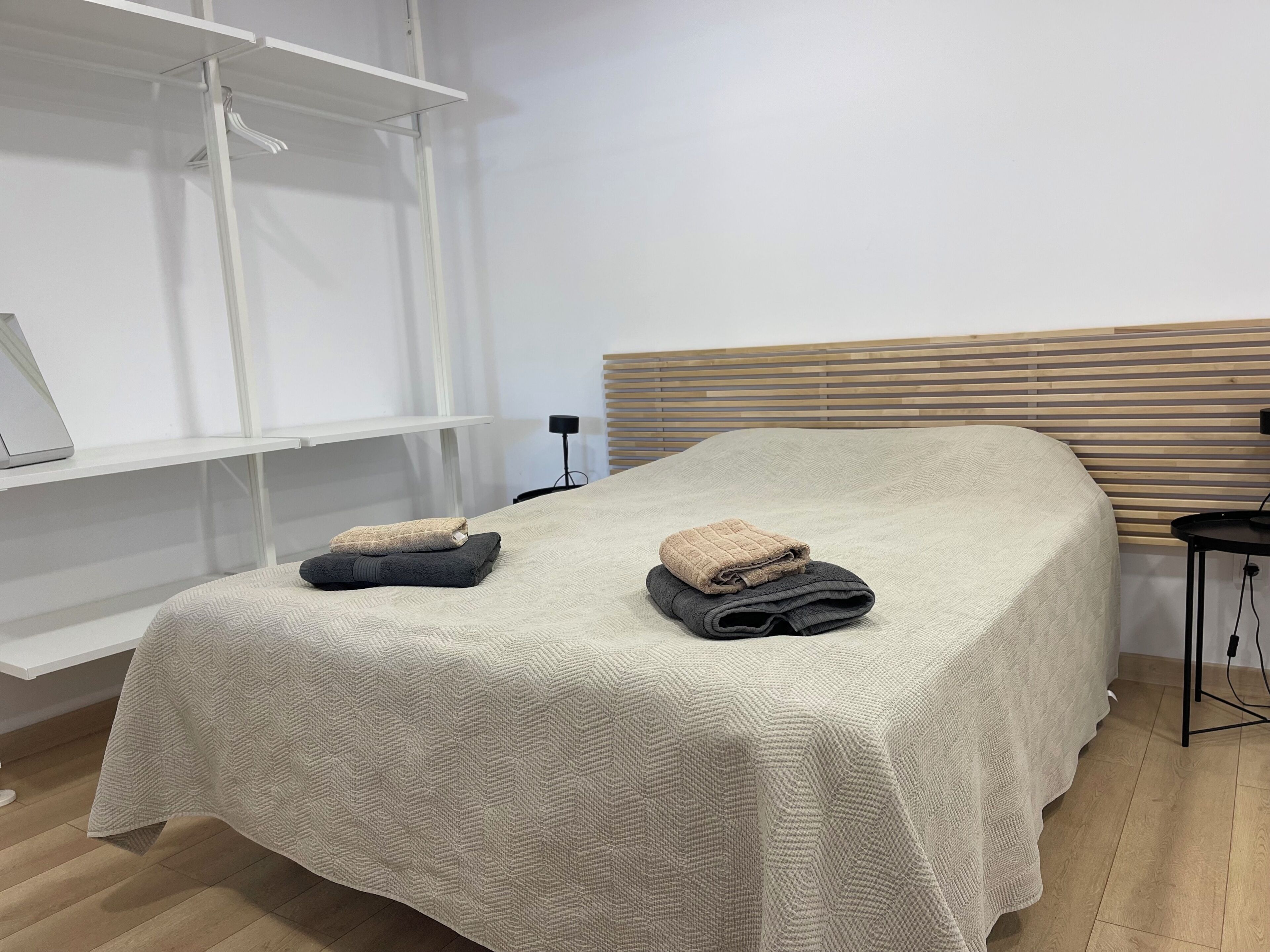 Un lit bien fait, avec une couvre-lit à motifs, deux serviettes pliées et une tête de lit en bois.
