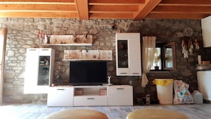 Ein Wohnzimmer mit Steinwand, Holzbalkendecke, Fernseher, weißen Schränken und einem Steinkamin.