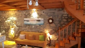 Ein gemütliches Zimmer mit Steinwand, einer Holztreppe und einer Couch mit Kissen.