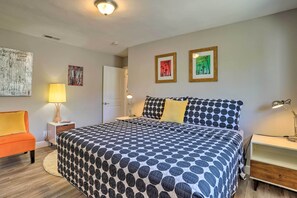 A bedroom with a large bed, a nightstand, a lamp, a chair, and artwork on the walls.